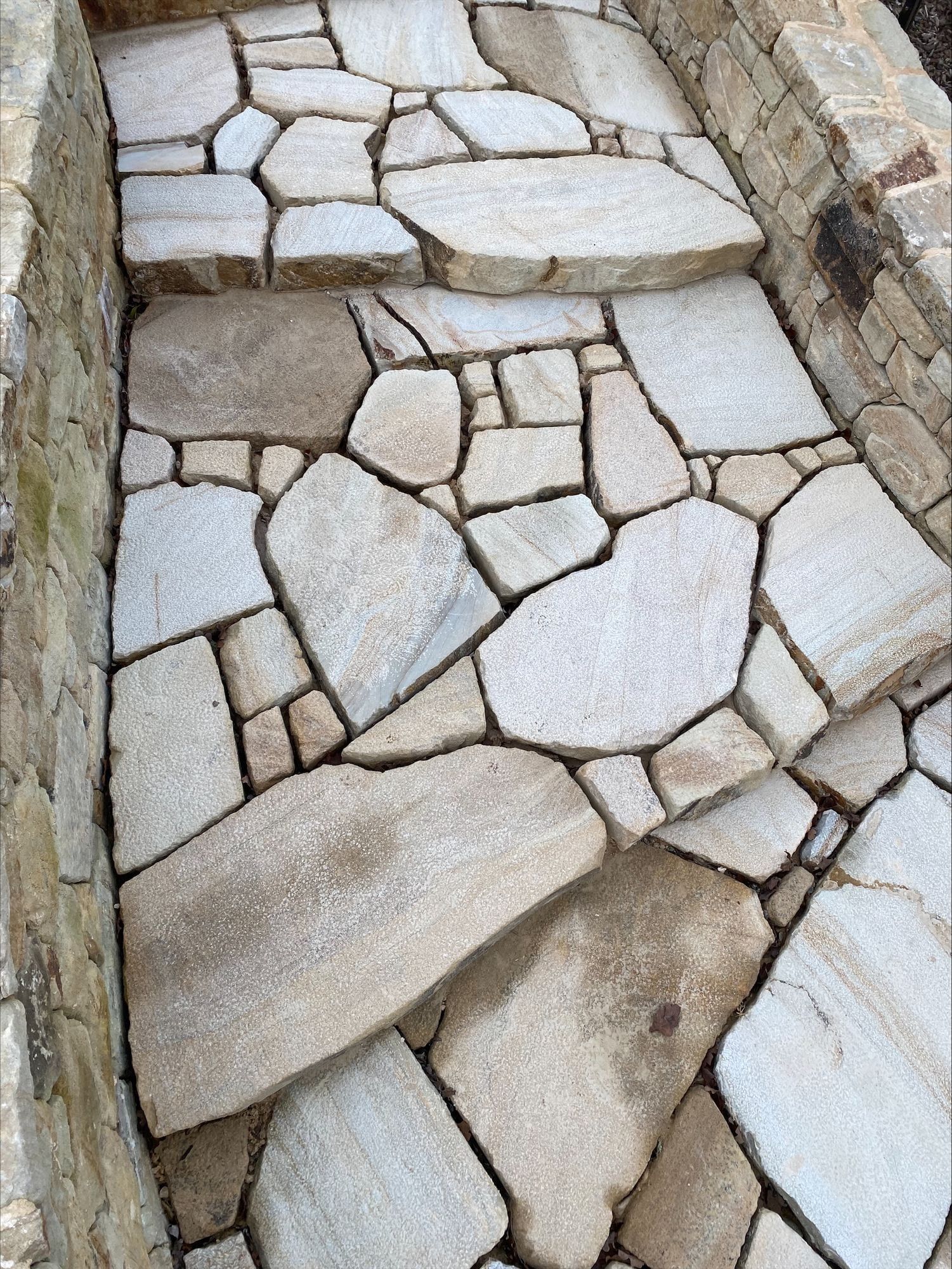 Crazy paving of pale sandstone beside a stone wall