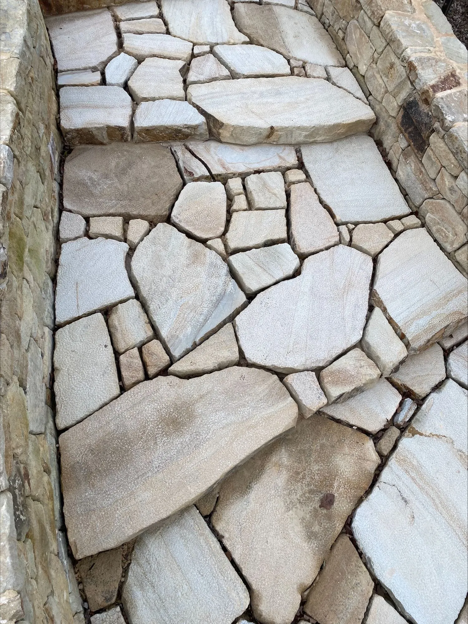 Crazy paving of pale sandstone beside a stone wall