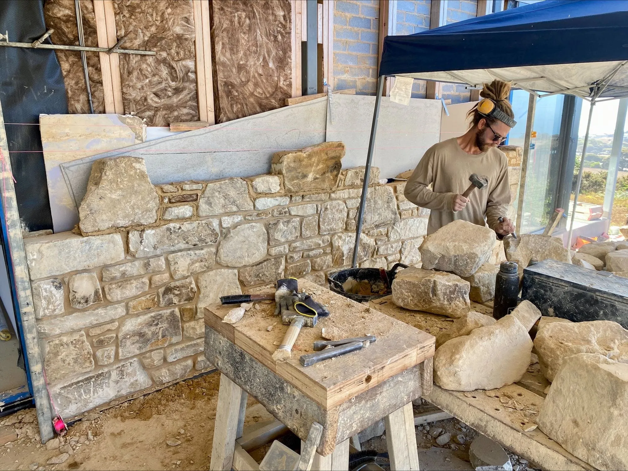 A mason shaping stone at a bench on a building site