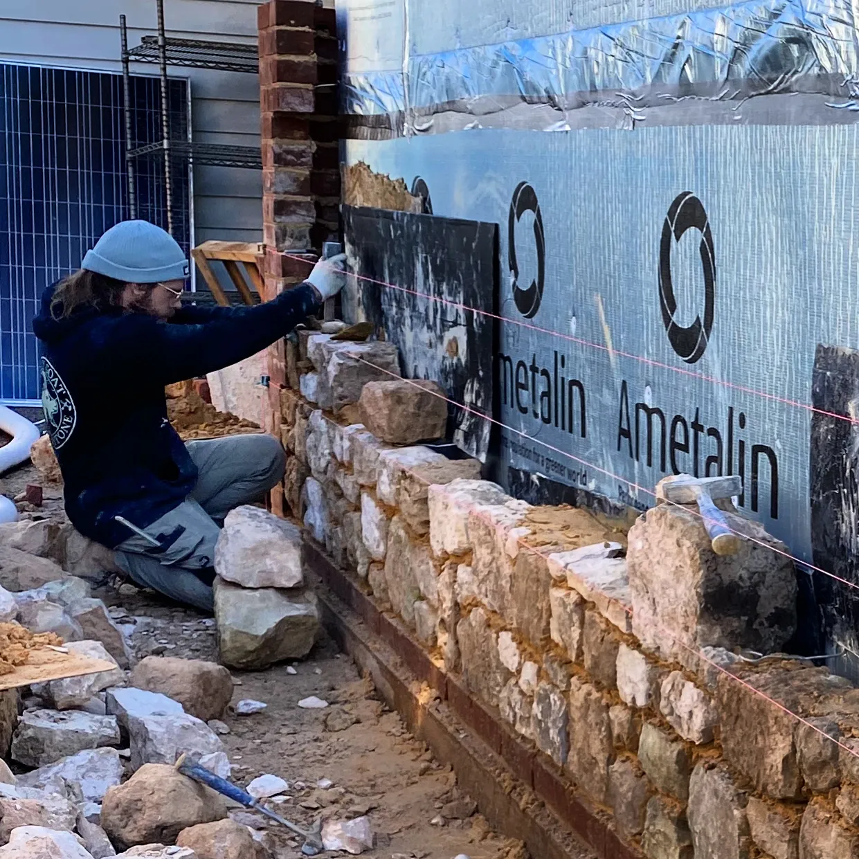 A mason laying a stone wall against a steel frame