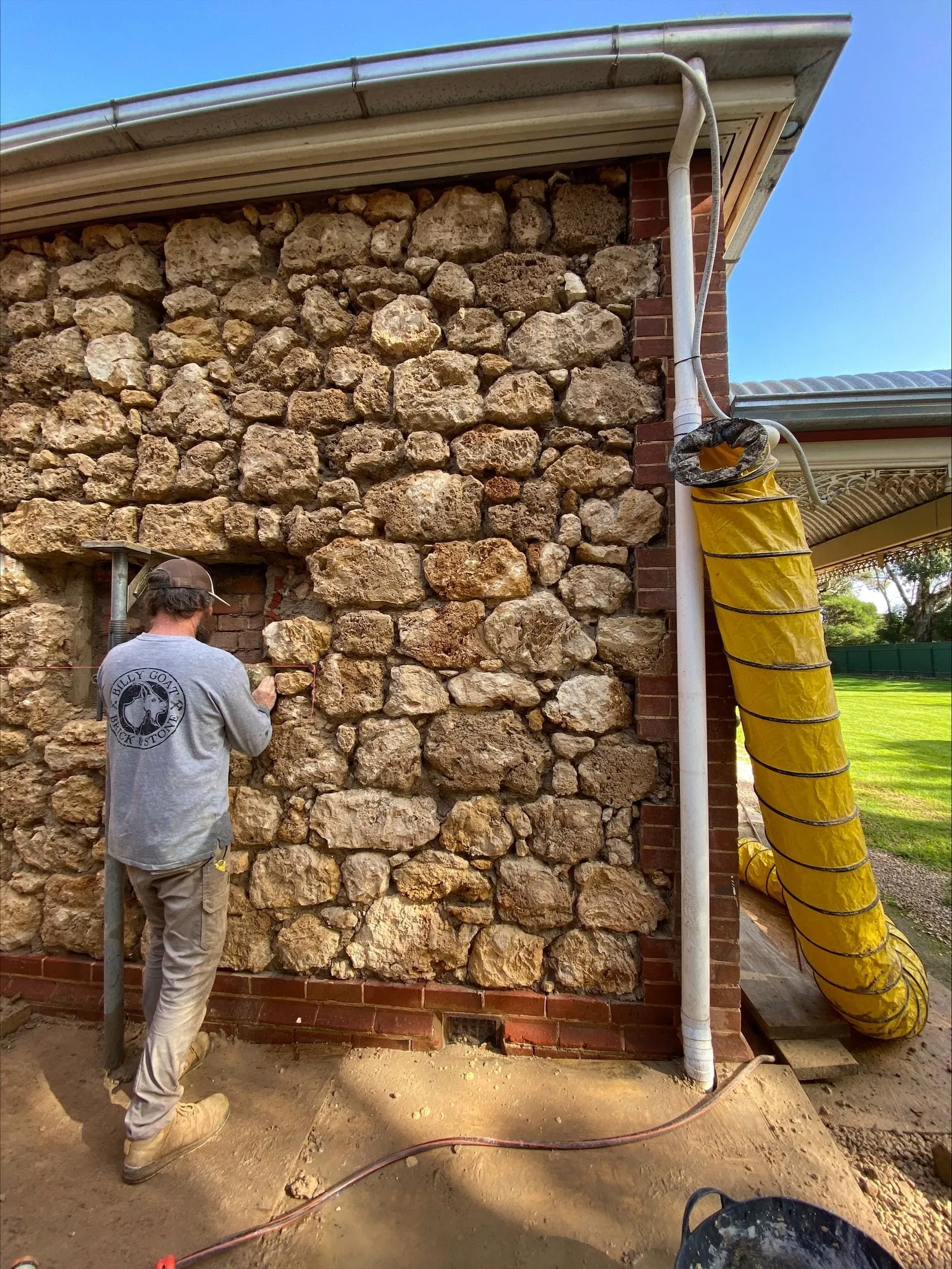 A rubble stone wall being built beside a house